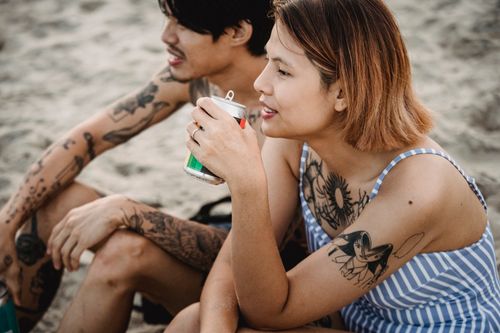 Free A tattooed couple enjoys a relaxing moment together on a sandy beach. Stock Photo