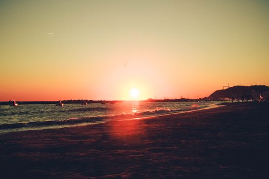 A serene beachscape at sunset with gentle waves and silhouetted boats on the horizon.