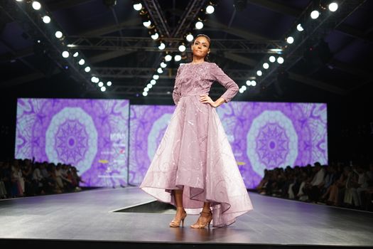 Model in elegant dress poses on a vibrant fashion show runway.