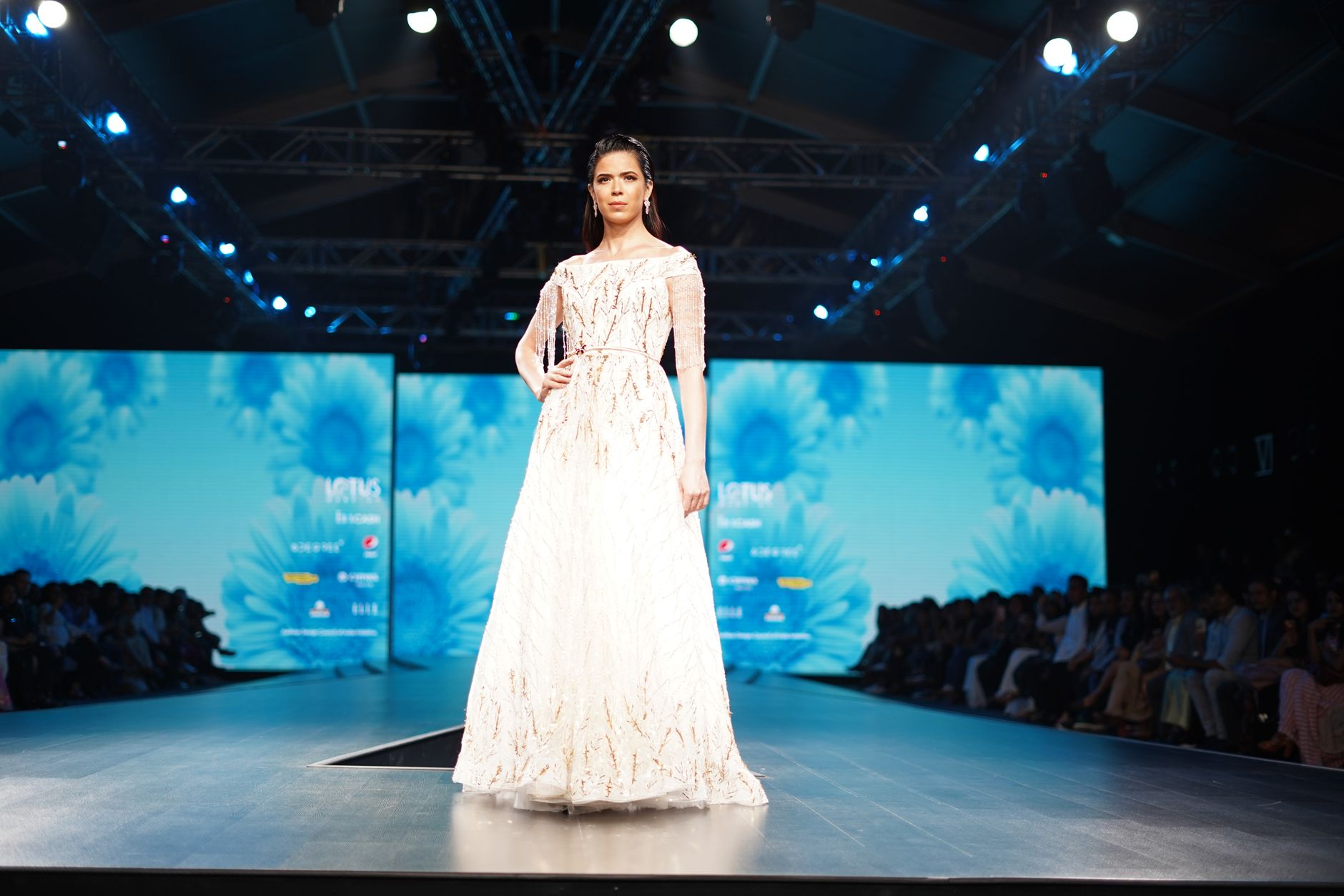 Model showcasing an elegant white dress on the runway during a high-fashion event.