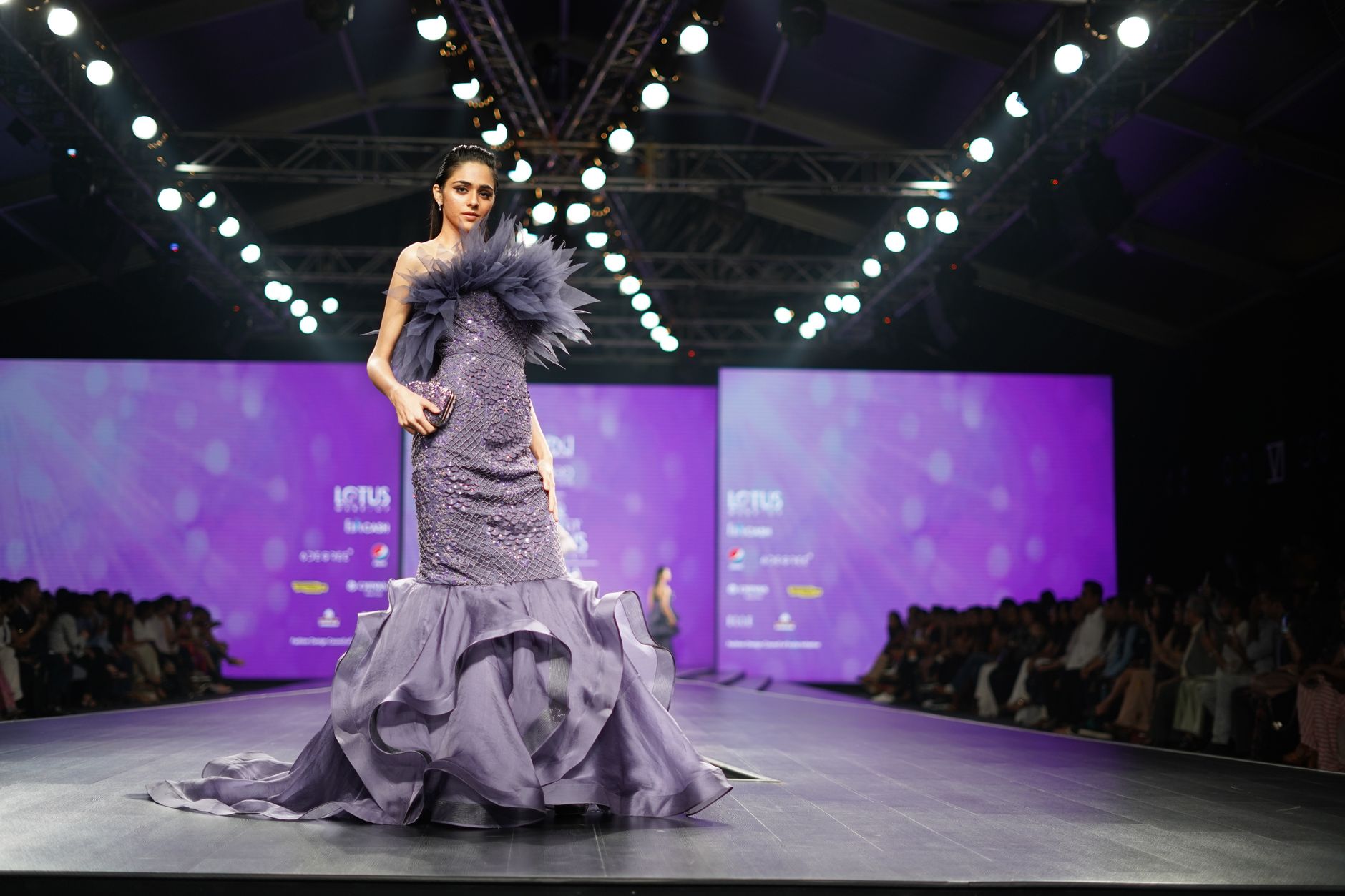 A model in a stunning purple gown walks the runway at a prestigious fashion event.