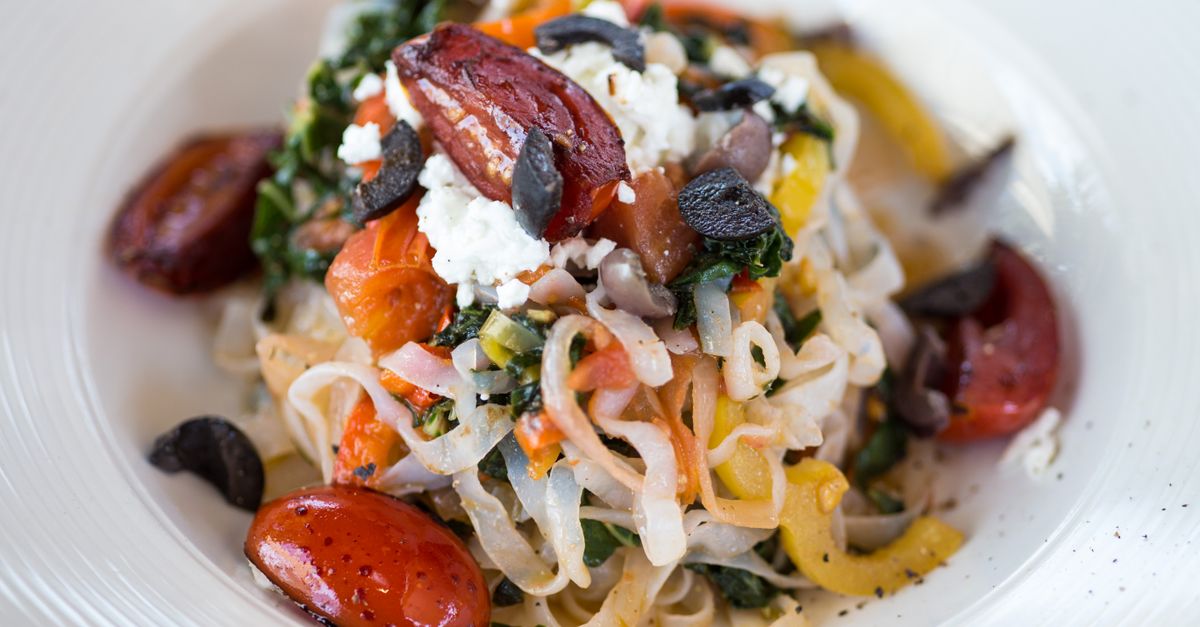 baked feta pasta with cherry tomatoes and herbs in a white baking dish
