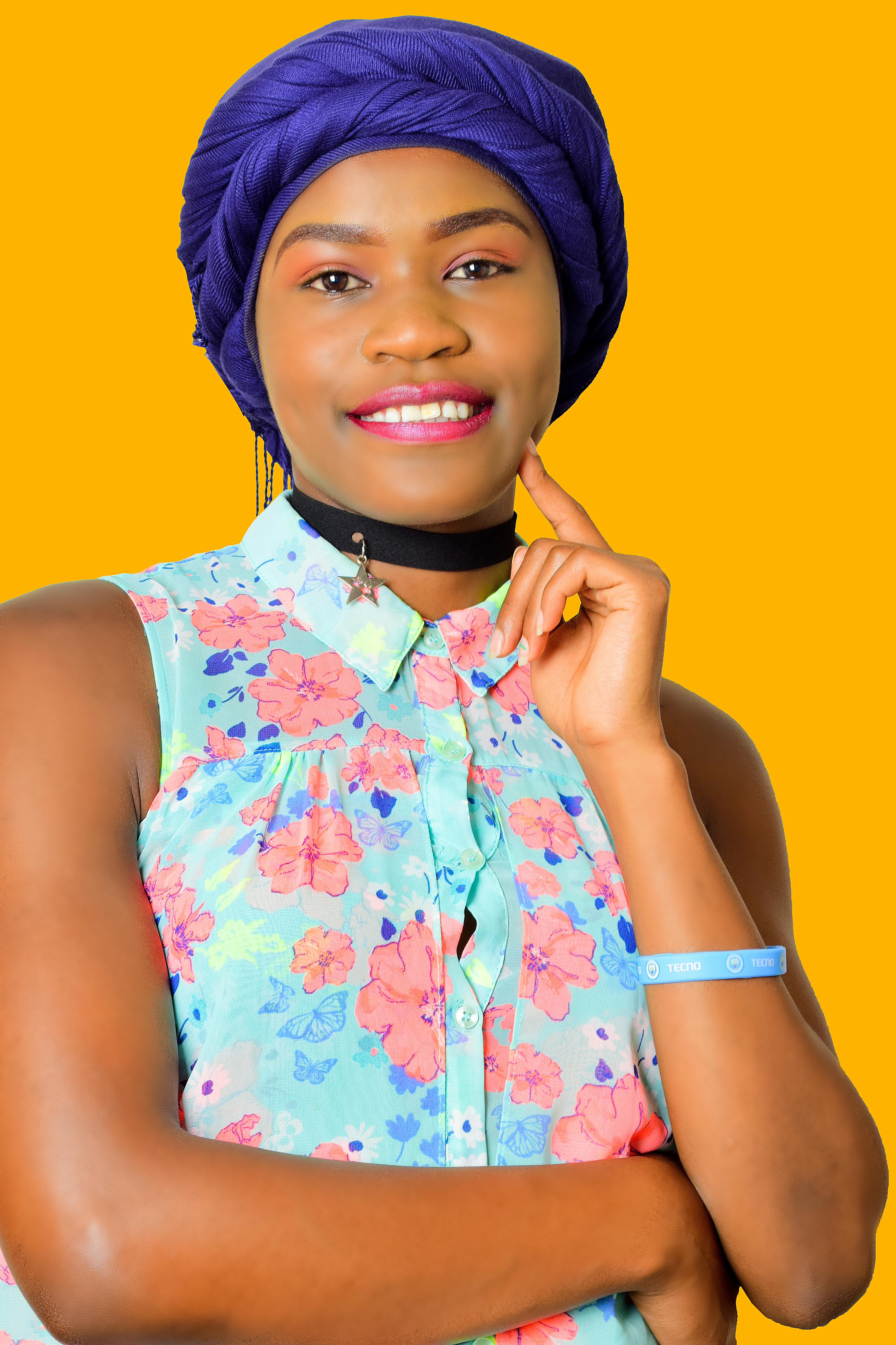 Bright portrait of a smiling woman in a floral shirt and headscarf on a vibrant yellow background.