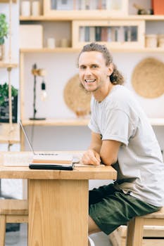 Smiling man with curly hair working on a laptop at home office, embracing remote work freedom.