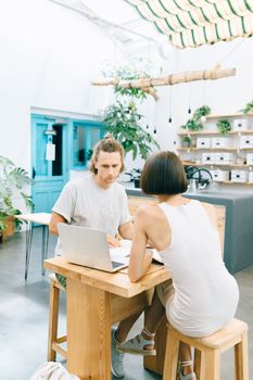 Two colleagues in a modern workspace having a discussion around a laptop.