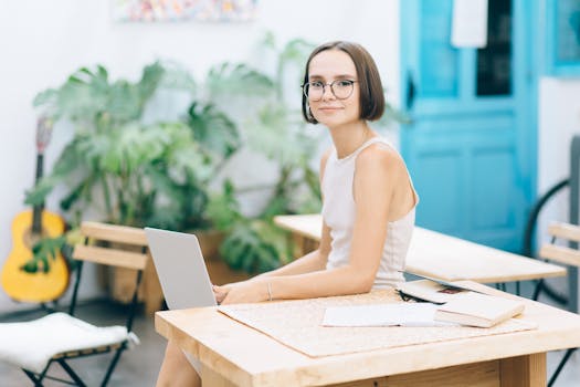 A young woman smiling while working remotely on her laptop in a bright, stylish workspace.