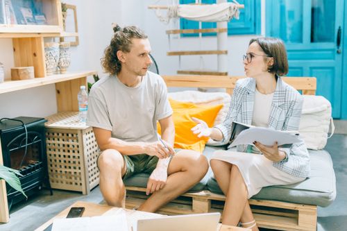 Free A man and woman discussing work in a stylish, bright living room setting. Stock Photo