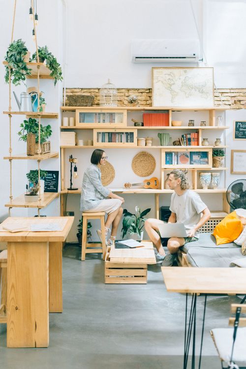 Free A bright modern workspace featuring two adults interacting in an open-plan office with plants and natural decor. Stock Photo