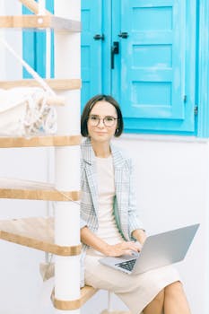 Stylish woman in glasses working remotely on a laptop in a bright indoor setting.