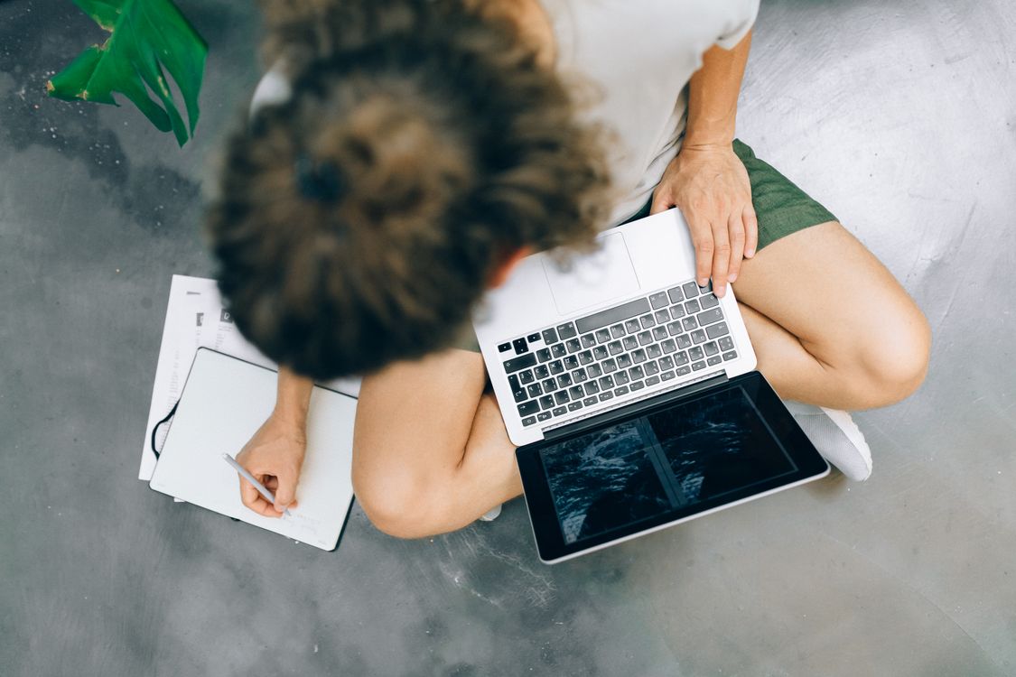 An overhead view of a person writing in a notebook beside an open laptop, representing the proposal drafting process
