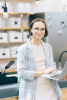 一位戴着眼镜、穿着格子外套、拿着笔记本电脑的女性在商务环境中微笑