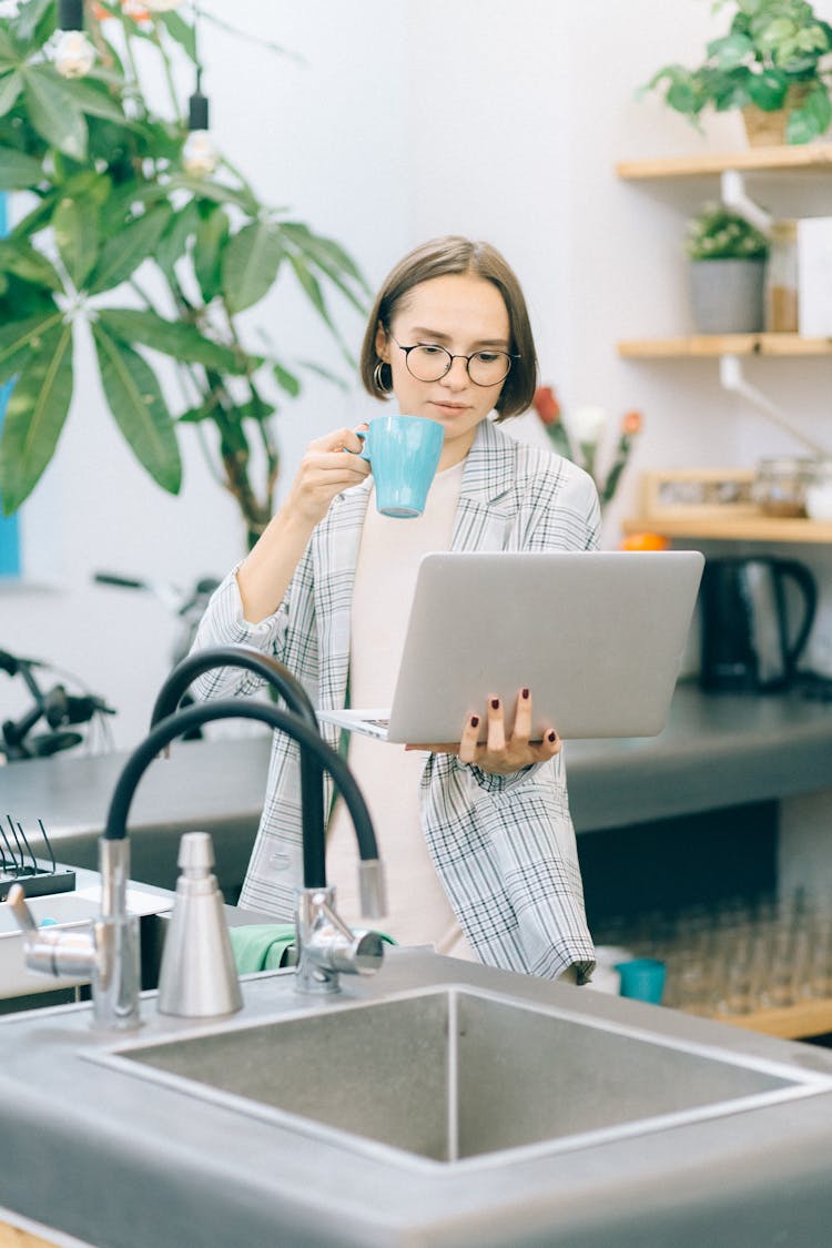 A Woman Drinking While Holding A Laptop