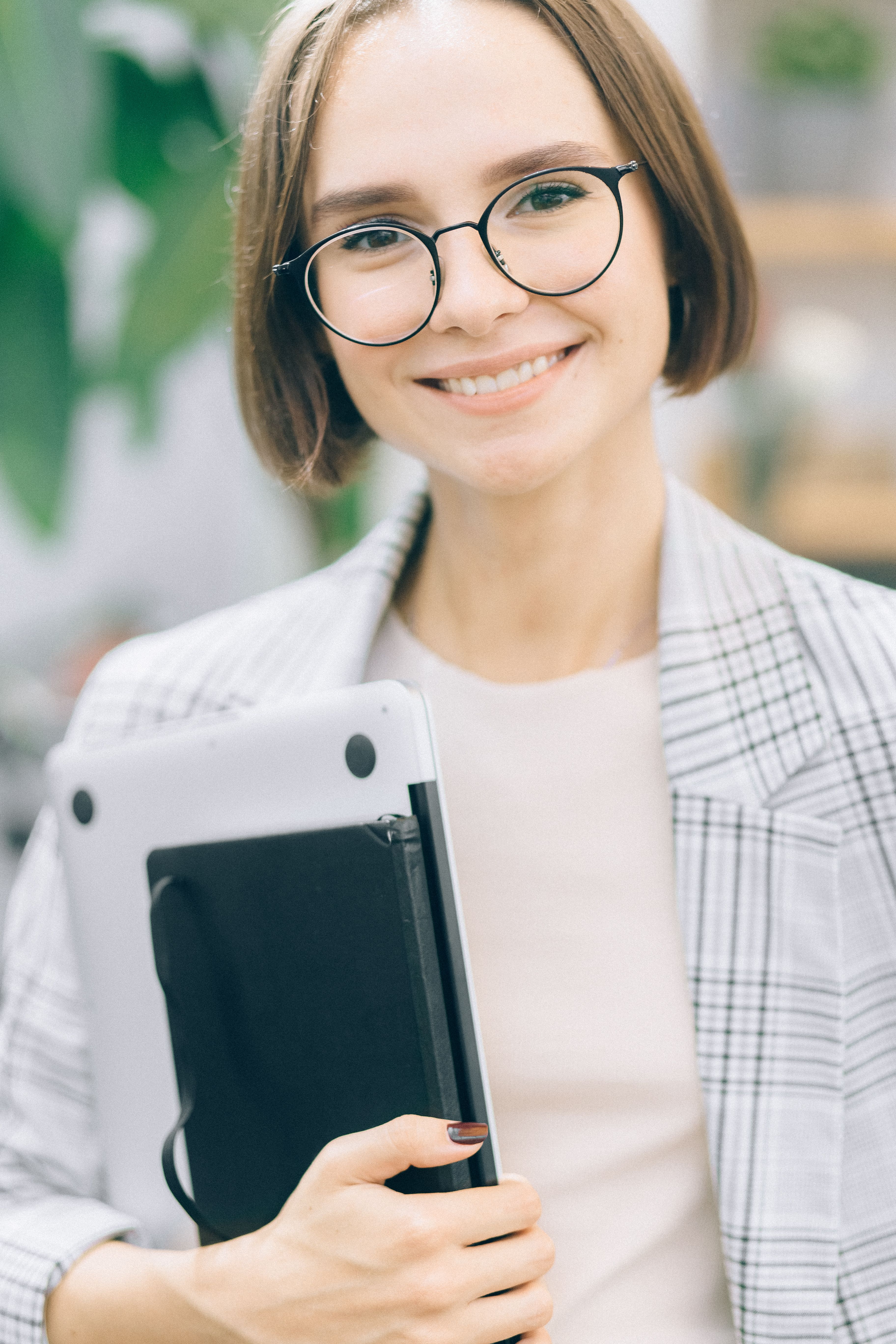 一位戴着眼镜、拿着笔记本电脑的自信女性在办公室环境中展现专业性