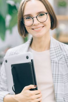 一位戴着眼镜、拿着笔记本电脑的自信女性在办公室环境中展现专业性
