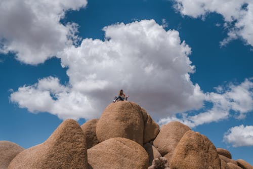 From below of unrecognizable female traveler relaxing in big rocky boulders against cloudy blue sky