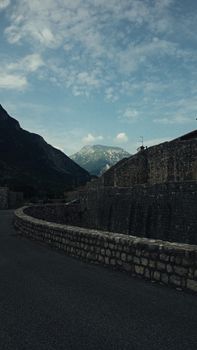 Scenery view of roadway with stone fence between high mounts under sky with clouds