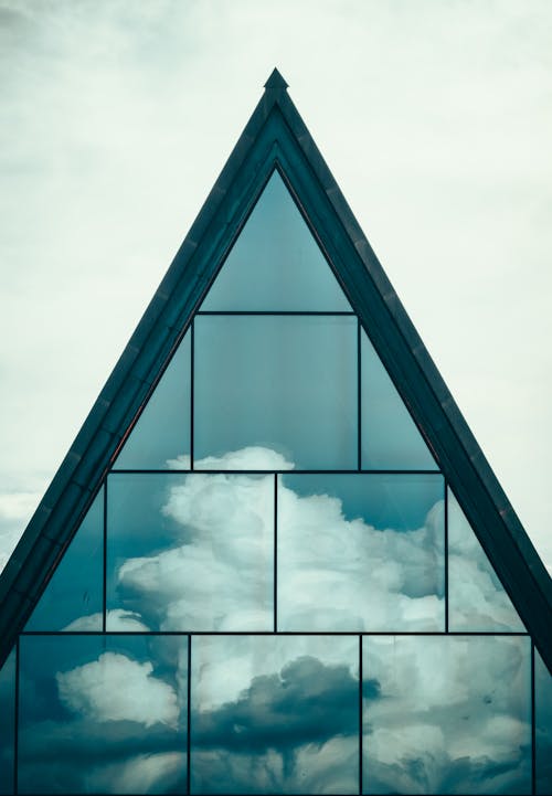 Modern residential building with geometric roof and clouds reflecting in clean mirrored surface