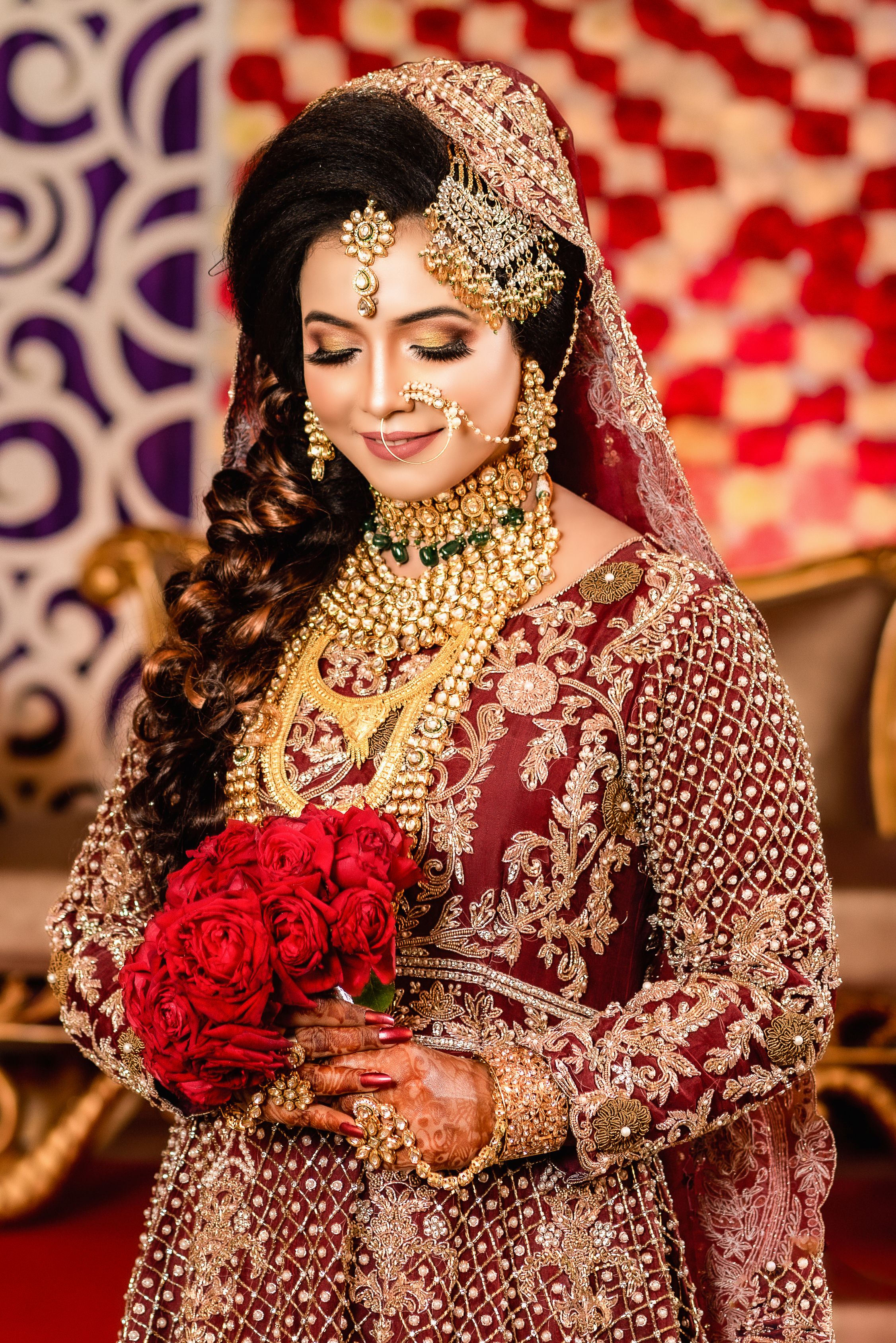 A beautiful South Asian bride in traditional attire with jewelry and bouquet of red roses.