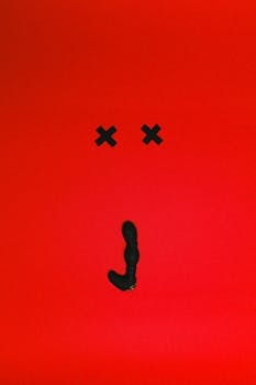 Artistic display of a black silicone vibrator on a vivid red background with cross marks.