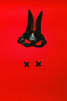 Conceptual image of a black leather rabbit mask on a bright red background, symbolizing mystery and allure.