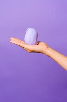 A minimalist image of a silicone toy held on an open hand against a bright purple backdrop.