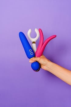 Vibrant sex toys being held against a purple backdrop, showcasing modern design.