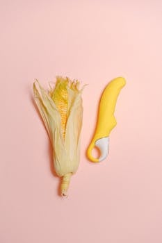 A creative still life featuring a corn cob and yellow silicone vibrator on a pastel background.
