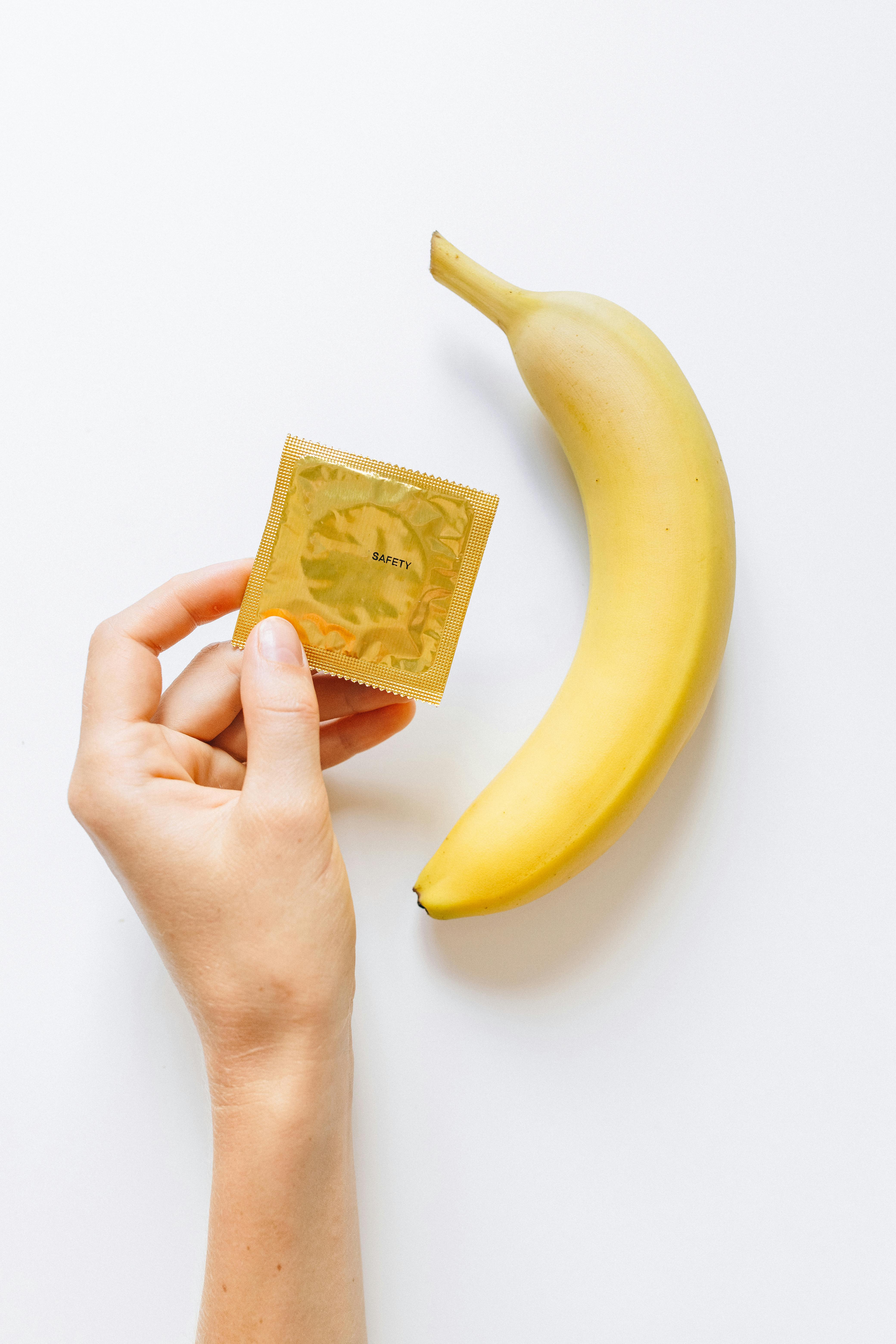 person holding condom next to banana