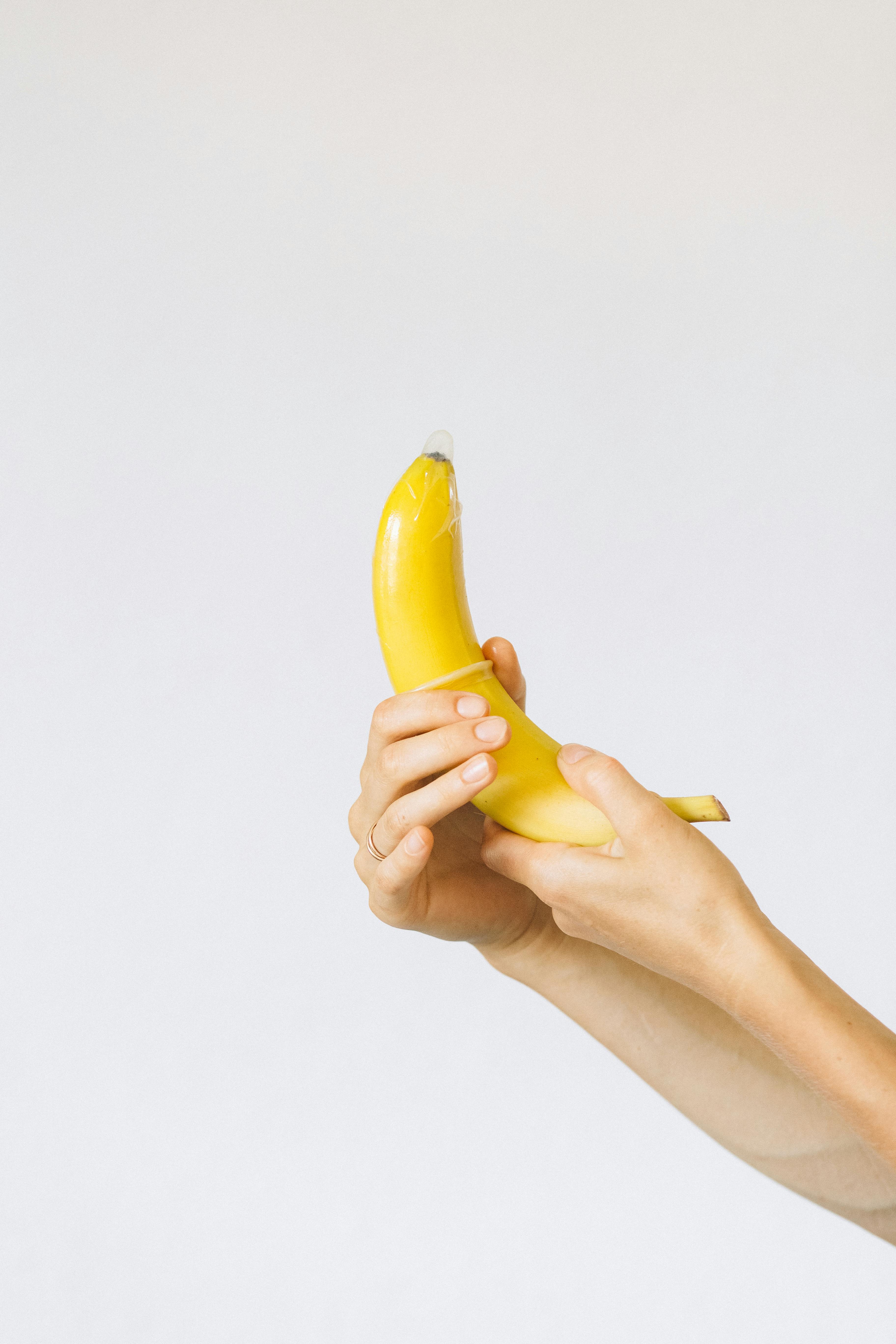 person wrapping condom on banana