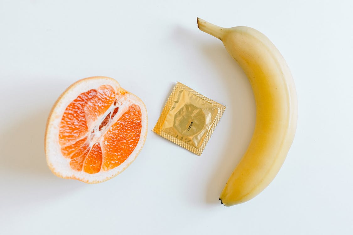Free Condom Between Orange and Banana Stock Photo