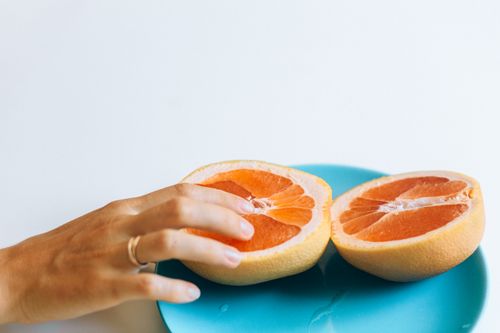 Free A hand gently touches grapefruit halves on a blue plate, symbolizing intimacy and freshness. Stock Photo
