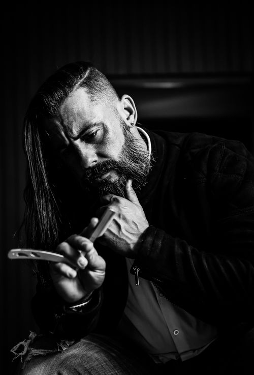 Free Dramatic black and white portrait of a bearded man with long hair and razor. Stock Photo