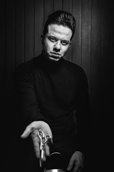 A dramatic black and white portrait of a man offering scissors, capturing a classic monochrome style.