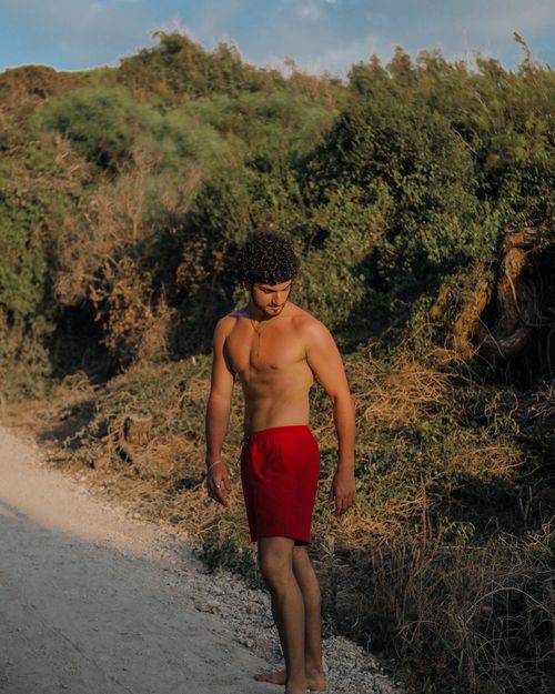 Free A shirtless man with curly hair walks on a sunny path in Paestum, Italy, showcasing natural beauty. Stock Photo