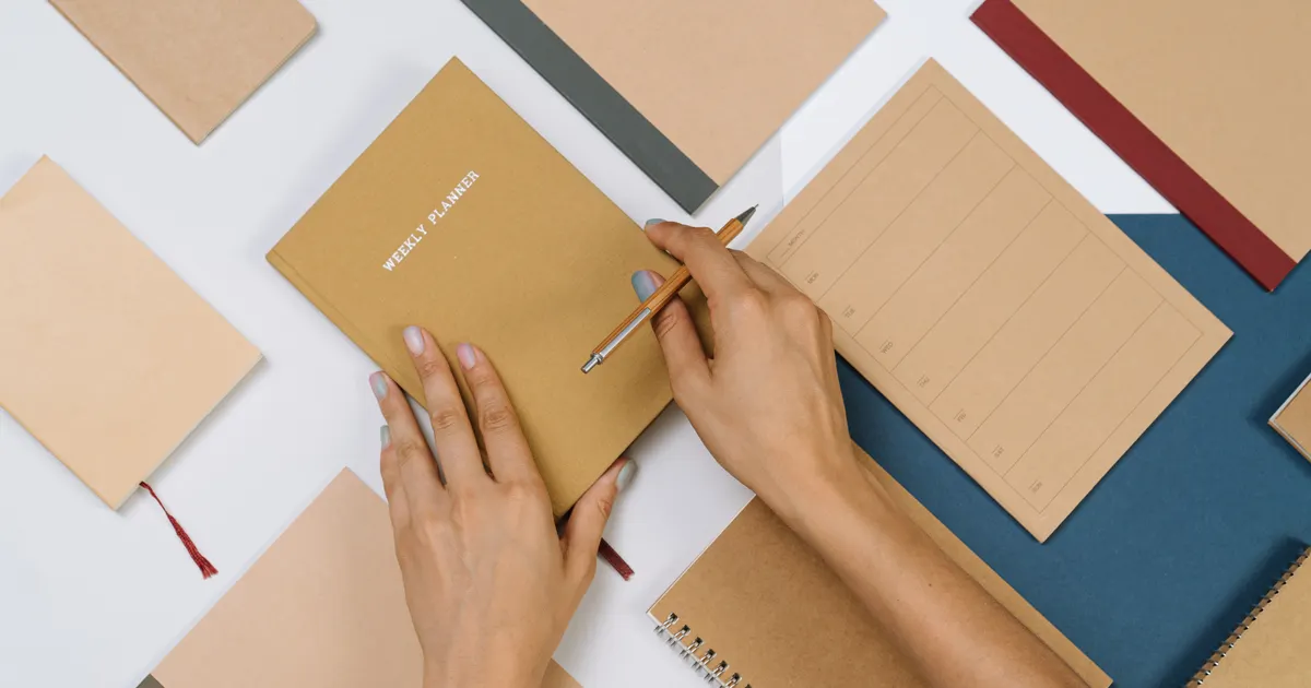 Hands writing in a weekly planner on a desk