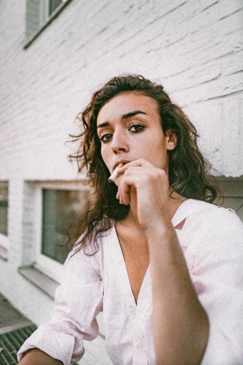 Free Stylish woman in pink blouse smoking outside a building in Brussels. Stock Photo