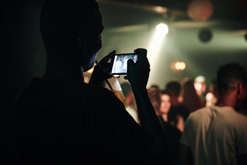 Silhouette of man photographing a vibrant club scene with smartphone.