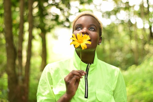 A Woman in Green Long Sleeve Shirt Holding a Yellow Flower