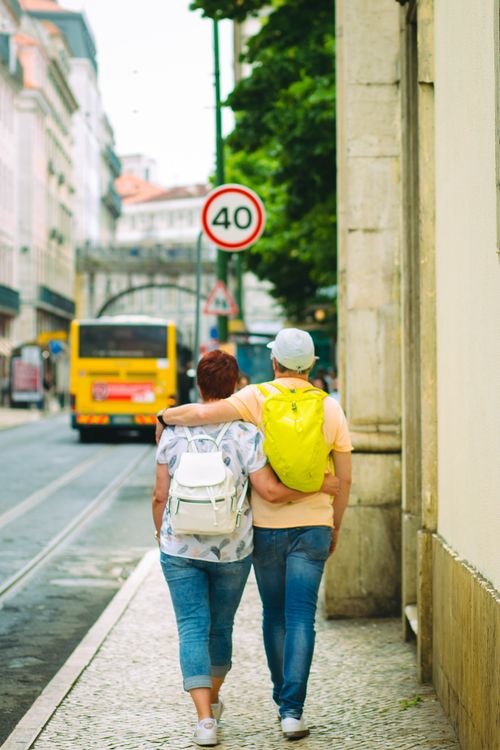 Free Back view full body of anonymous couple with backpacks in casual clothes embracing and strolling along narrow street Stock Photo