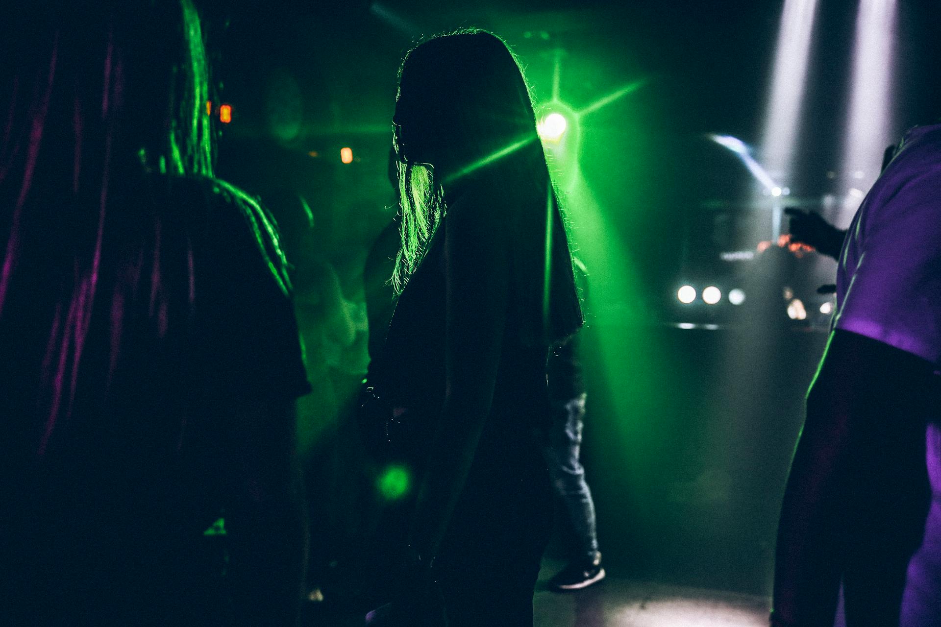 Silhouettes of people dancing under colorful lights in a lively nightclub.