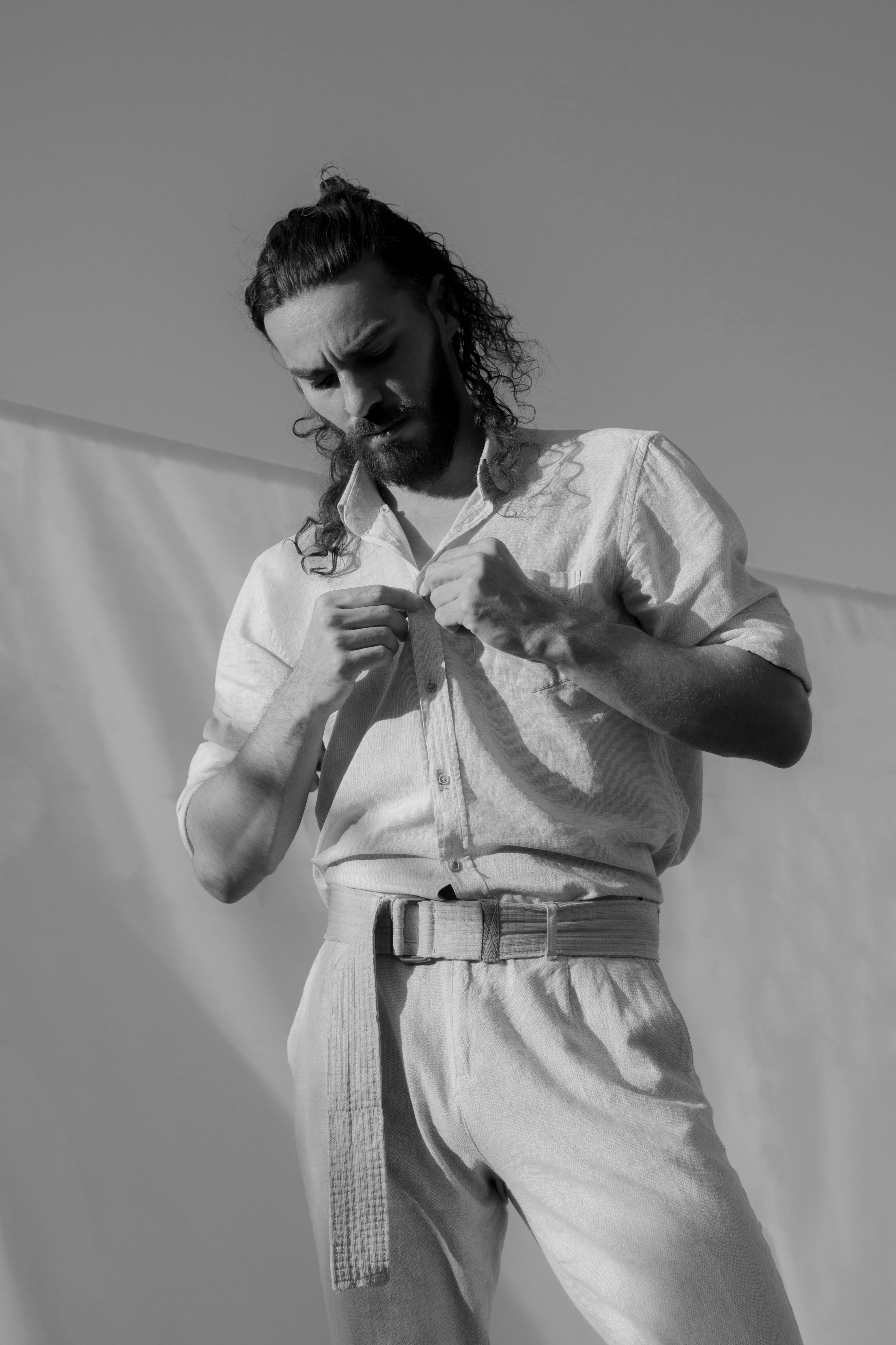 Black and white of busy pensive male buttoning shirt in sunny clear weather