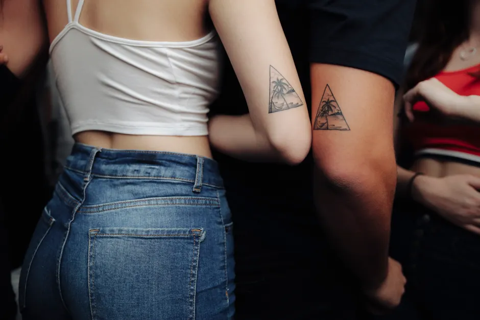 Two friends showing matching triangle-framed geometric temporary tattoos on their arms