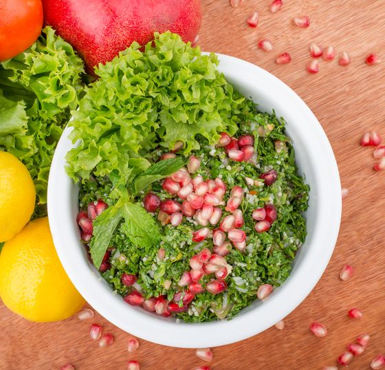 White bowl of parsley tabbouleh with pomegranate seeds, mint leaves and frilly lettuce