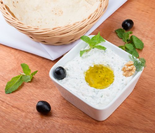 Free A close-up of creamy tzatziki dip with olive oil, herbs, and bread in a basket. Stock Photo