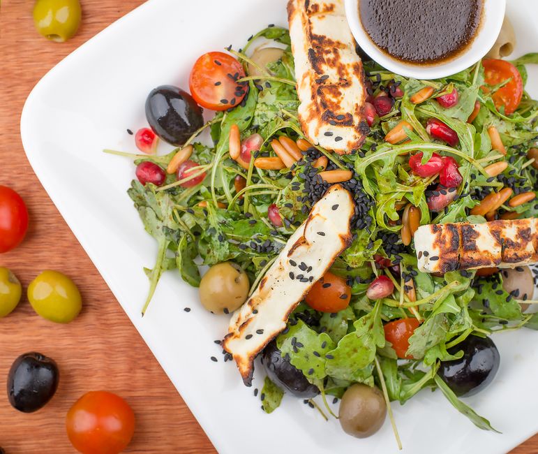 Close-up of grilled Halloumi cheese served on a plate with herbs.