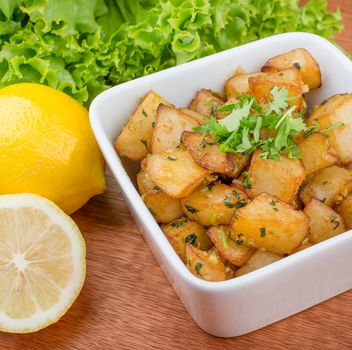 Delicious crispy batata harra served with fresh lemon and green garnish in a square bowl.