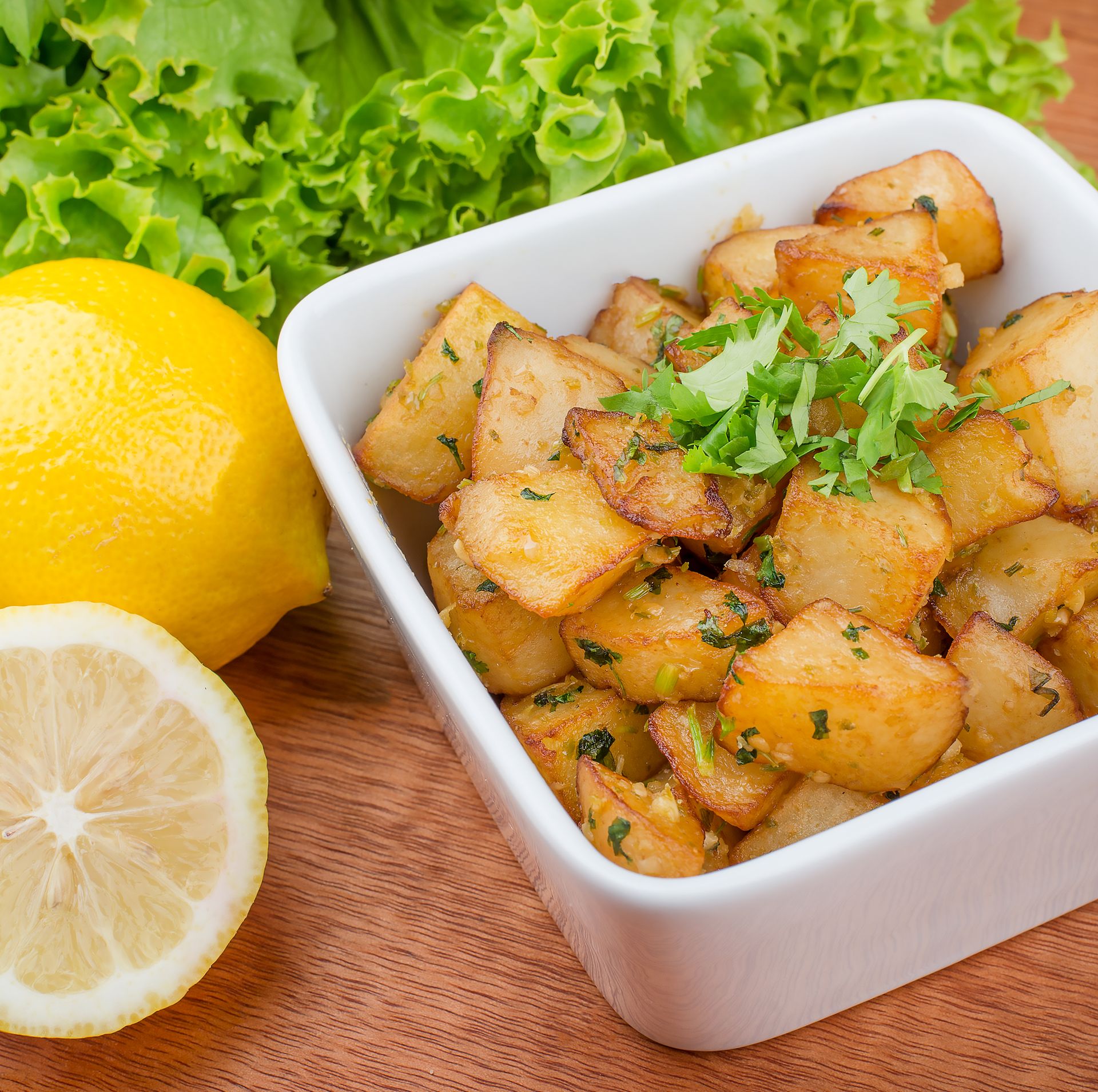 Delicious crispy batata harra served with fresh lemon and green garnish in a square bowl.