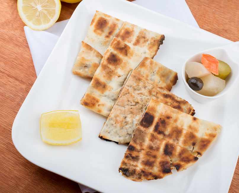 Grilled arayes cut in half showing a crisp charred pita crust packed with seasoned ground meat, served with a side of tahini sauce and lemon wedges.