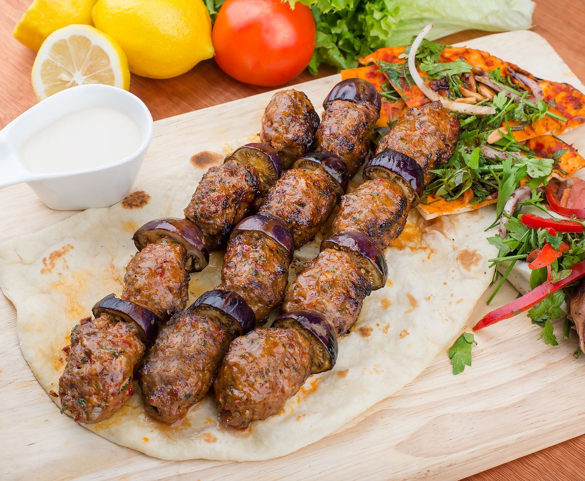 Grilled meatball and eggplant round skewers on lavash with lemon, tahini sauce and arugula salad