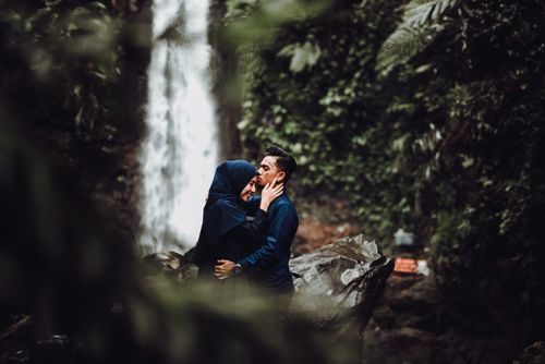 Free A couple sharing a romantic moment near a waterfall in a lush forest setting, embracing affectionately. Stock Photo